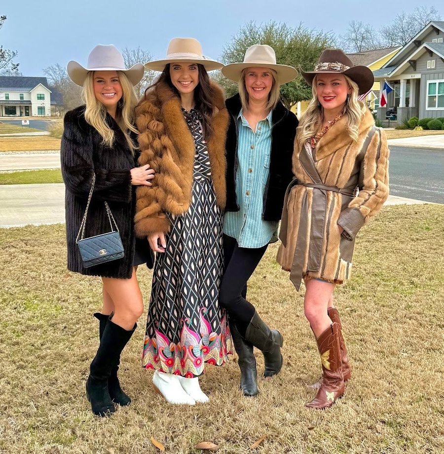 Four friends in felt hats, boots and cozy coats standing on a front lawn in Fredericksburg