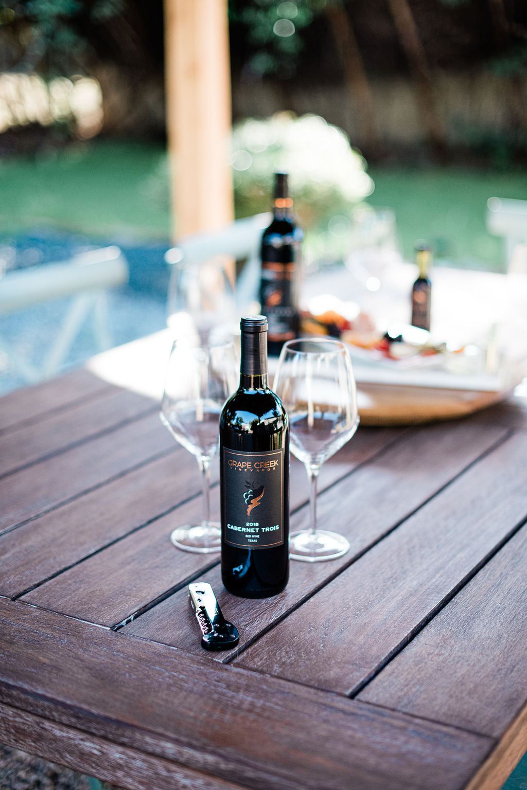 A bottle of Grape Creek red wine and two glasses on an outdoor table