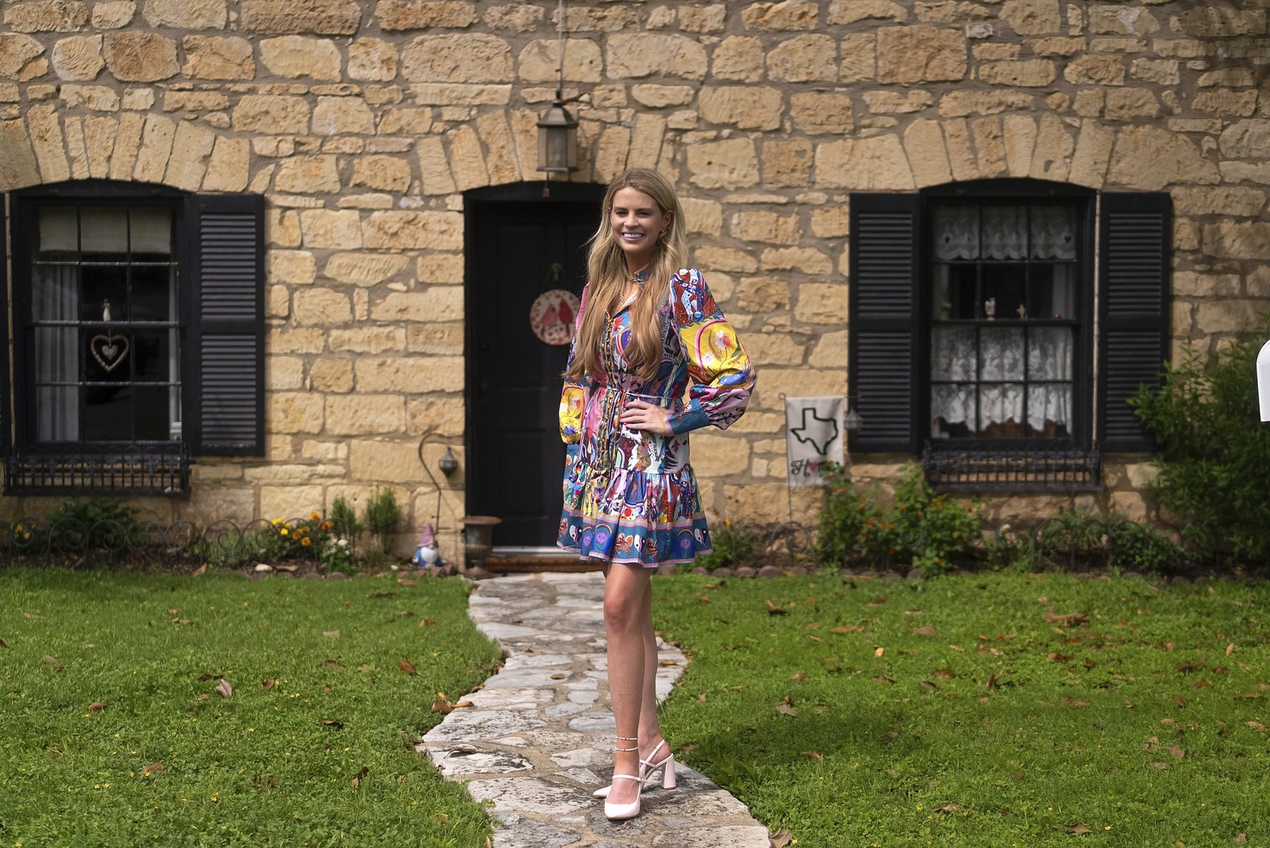 Savannah Sikes in a colorful print dress in front of a historic limestone home in Fredericksburg