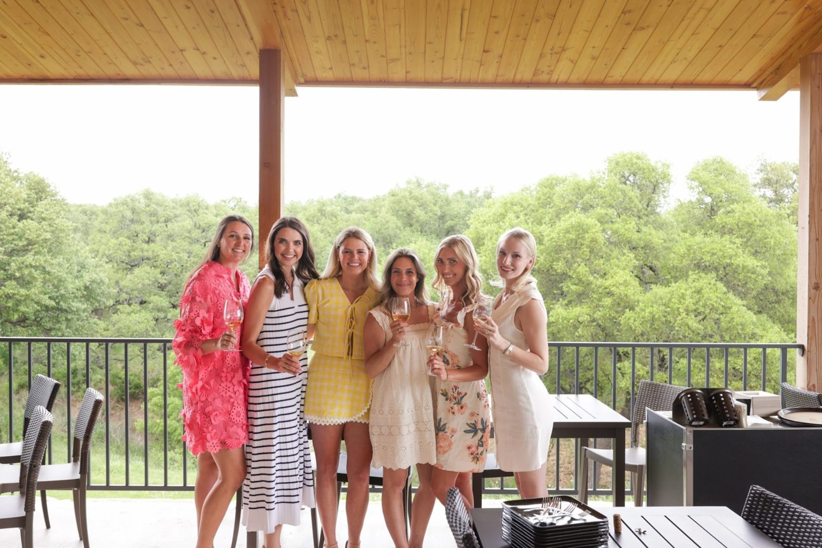 Friends with glasses of white wine on a winery porch overlooking the Hill Country