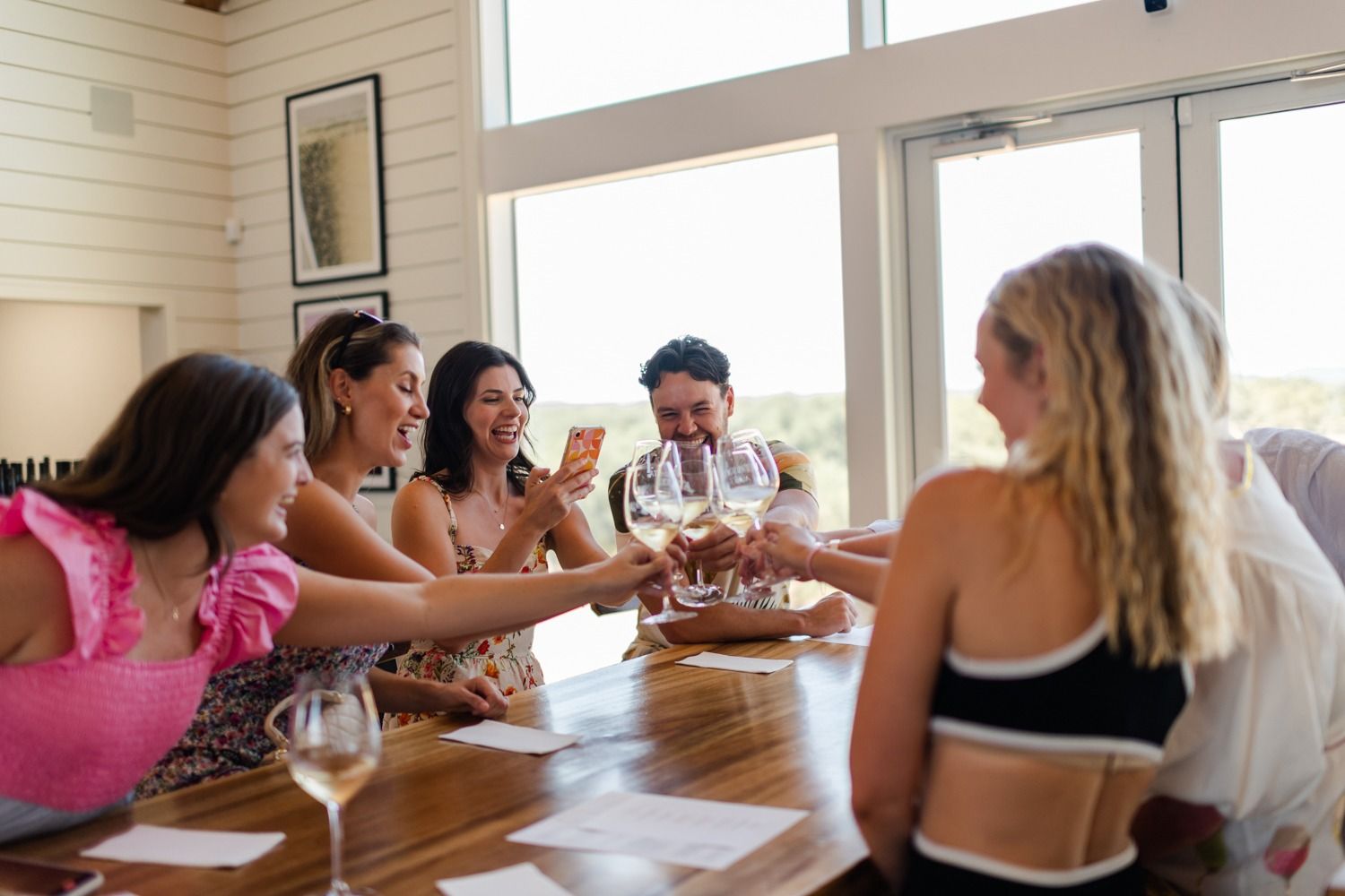Friends raising their glasses around a tasting table in a bright Hill Country tasting room